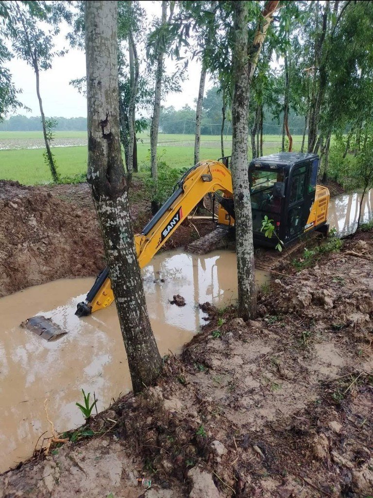 Excavator working in wet ground among trees