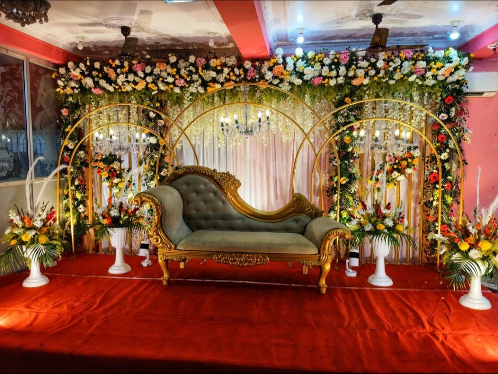 Indoor wedding stage with gold floral arches and a chaise
